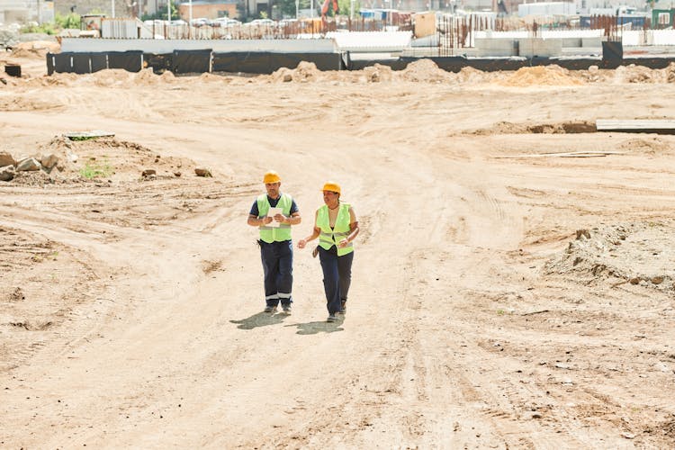 Man And Woman In Helmets And Reflective Vests Walking On A Construction Site