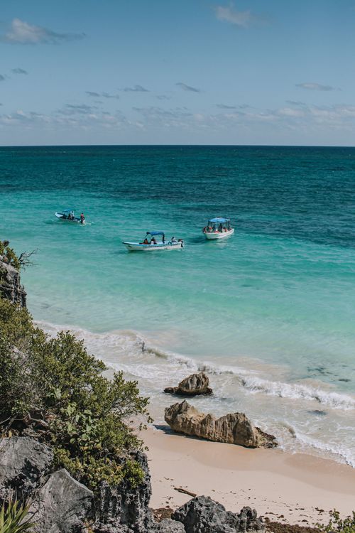 Free A breathtaking view of Tulum's beach with boats on turquoise waters and rocky shoreline. Stock Photo