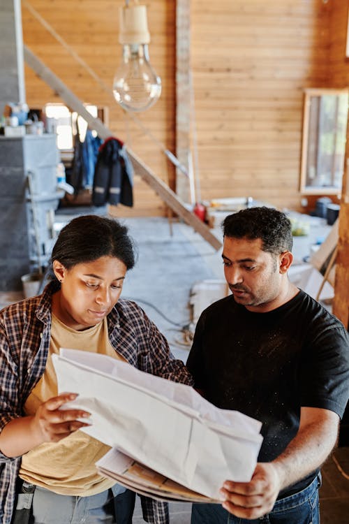 Man in Black Crew Neck T-shirt Standing Beside Woman in Plaid Shirt Looking on a Plan