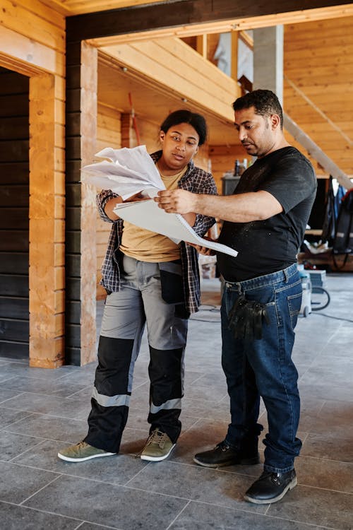 Construction Workers Looking at Papers while Standing in a Wooden House 