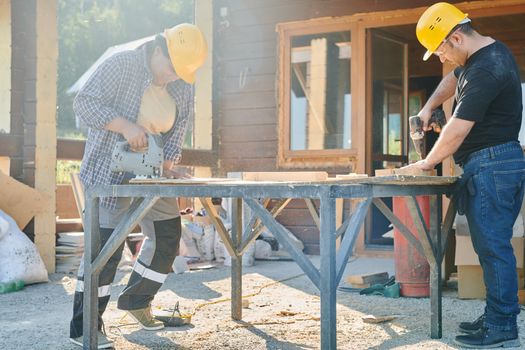 Two construction workers using power tools on a sunny day.