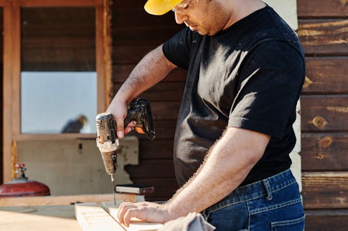 Free A Man Wearing Black Shirt and Hard Hat Holding a Power Tool Stock Photo