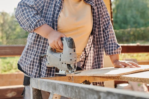 Person in Yellow Shirt and Blue and White Plaid Button Up Shirt Holding Black and Gray Hand Tool