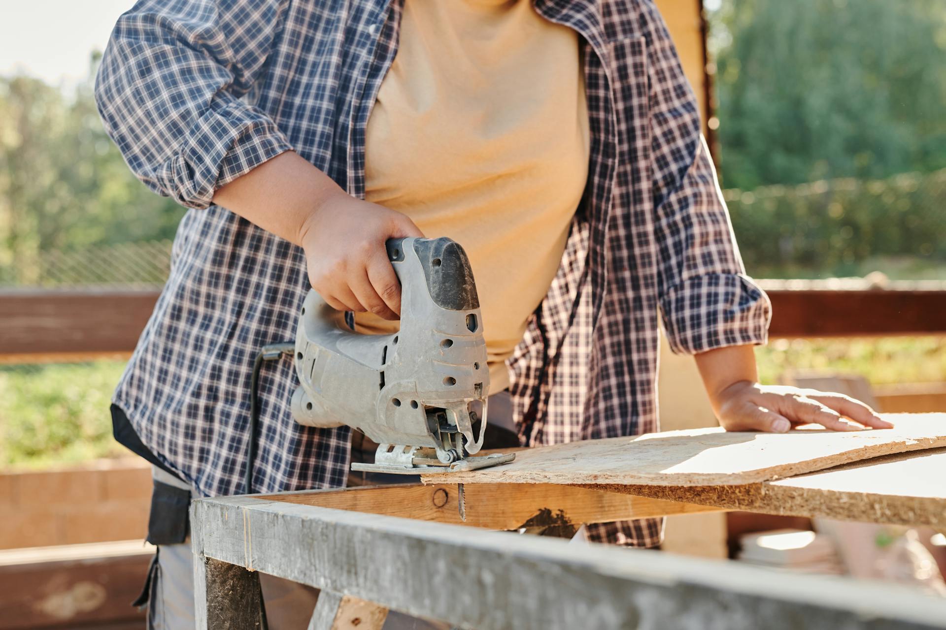 A carpenter using a jigsaw to cut plywood at a construction site. Outdoor setting.