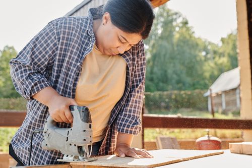 Free Focused woman using a jigsaw to cut wood outdoors. Ideal for carpentry, construction themes. Stock Photo