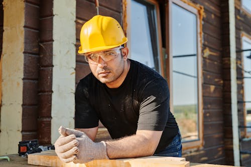 Man in Black Crew Neck T-shirt Wearing Yellow Hard Hat While Standing by the Wooden Table