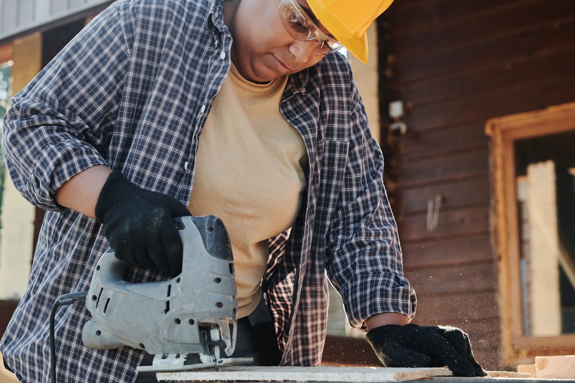 A focused construction worker using an electric jigsaw on wood outdoors.