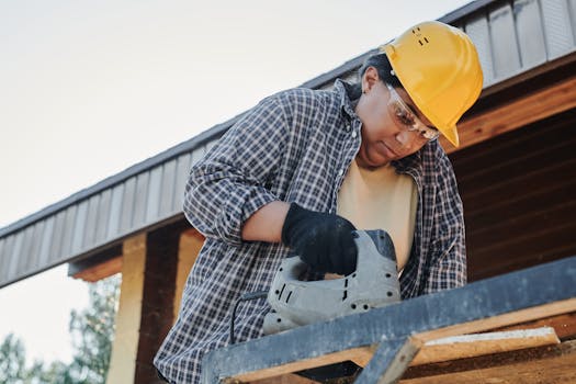 A woman carpenter uses a circular saw at a construction site wearing safety gear.
