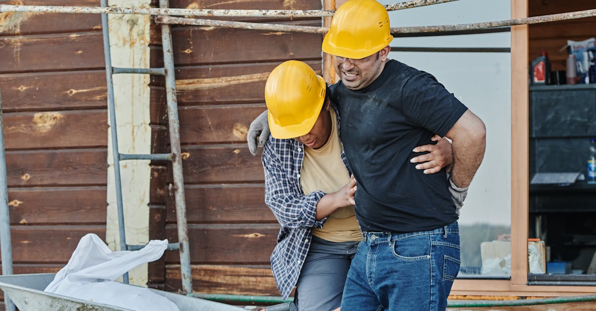 Photo by Mikael Blomkvist Construction workers wearing helmets assist an injured colleague at a building site with wooden cabins.