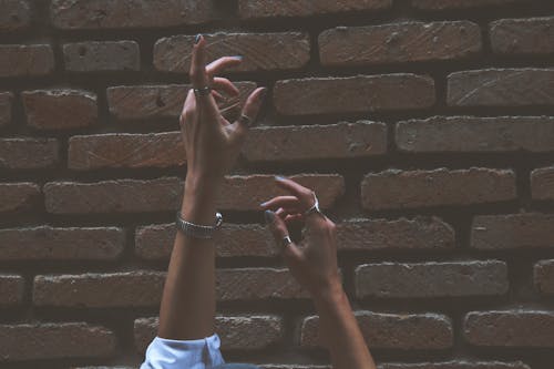 Free Person Raising Its Two Hand Beside Brown Brick Wall Stock Photo