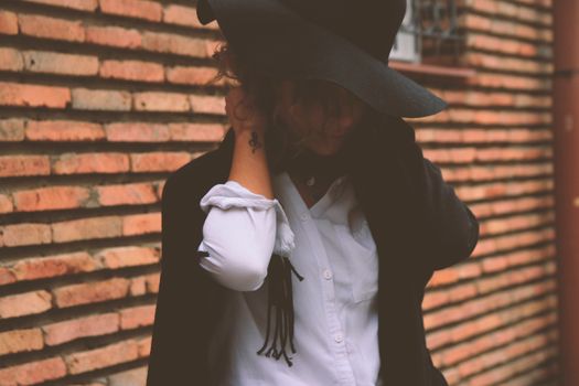 Fashionable woman in a hat posing against a brick wall, embracing modern urban style.