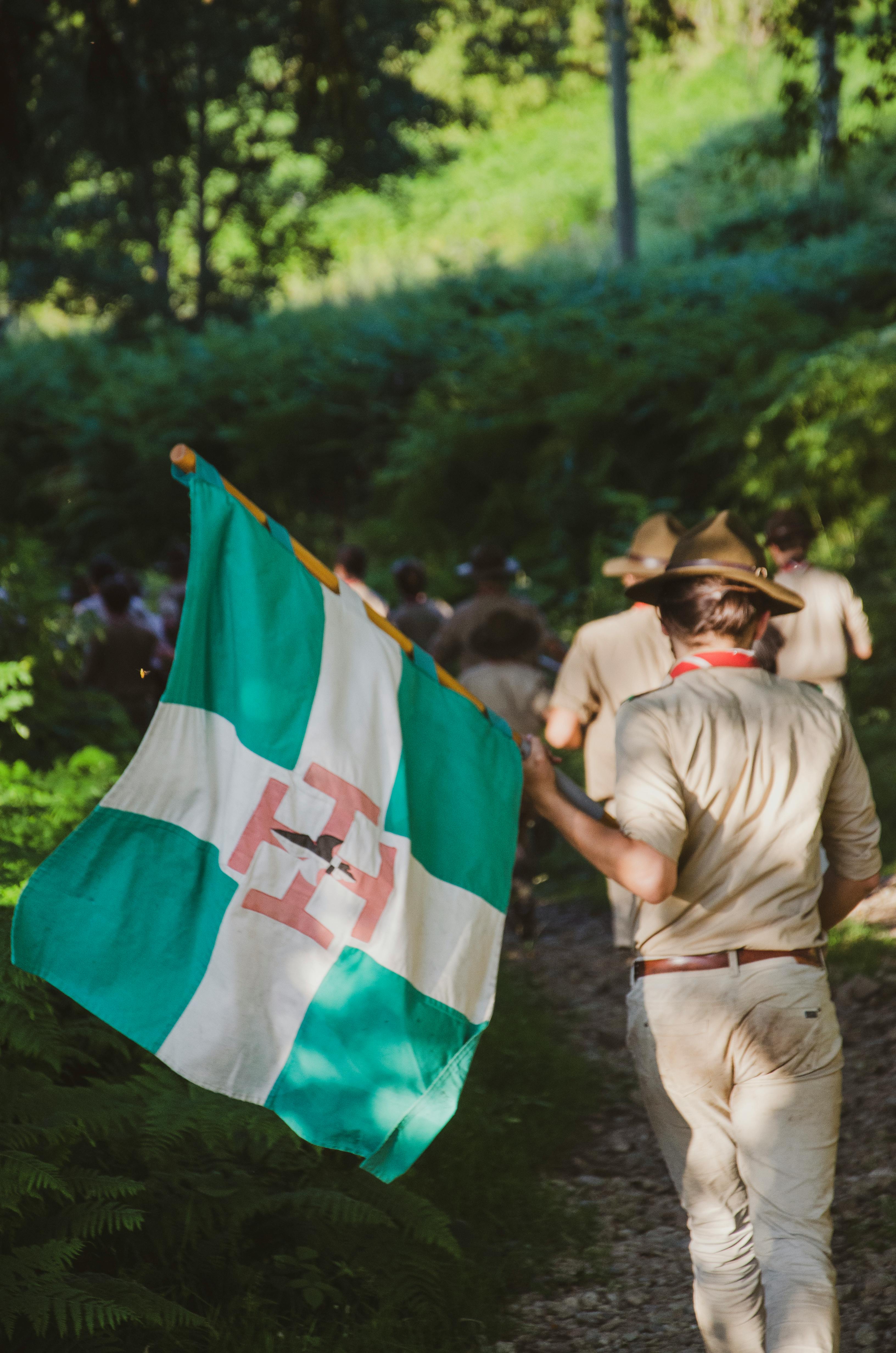 Boy scouts on a trail hike in the forest holding a flag.
