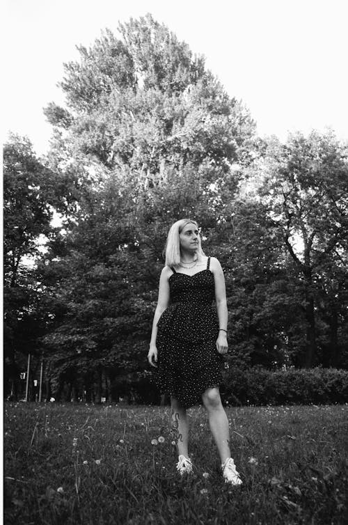 Grayscale Photo of a Woman in a Dress Standing on a Grassy Field