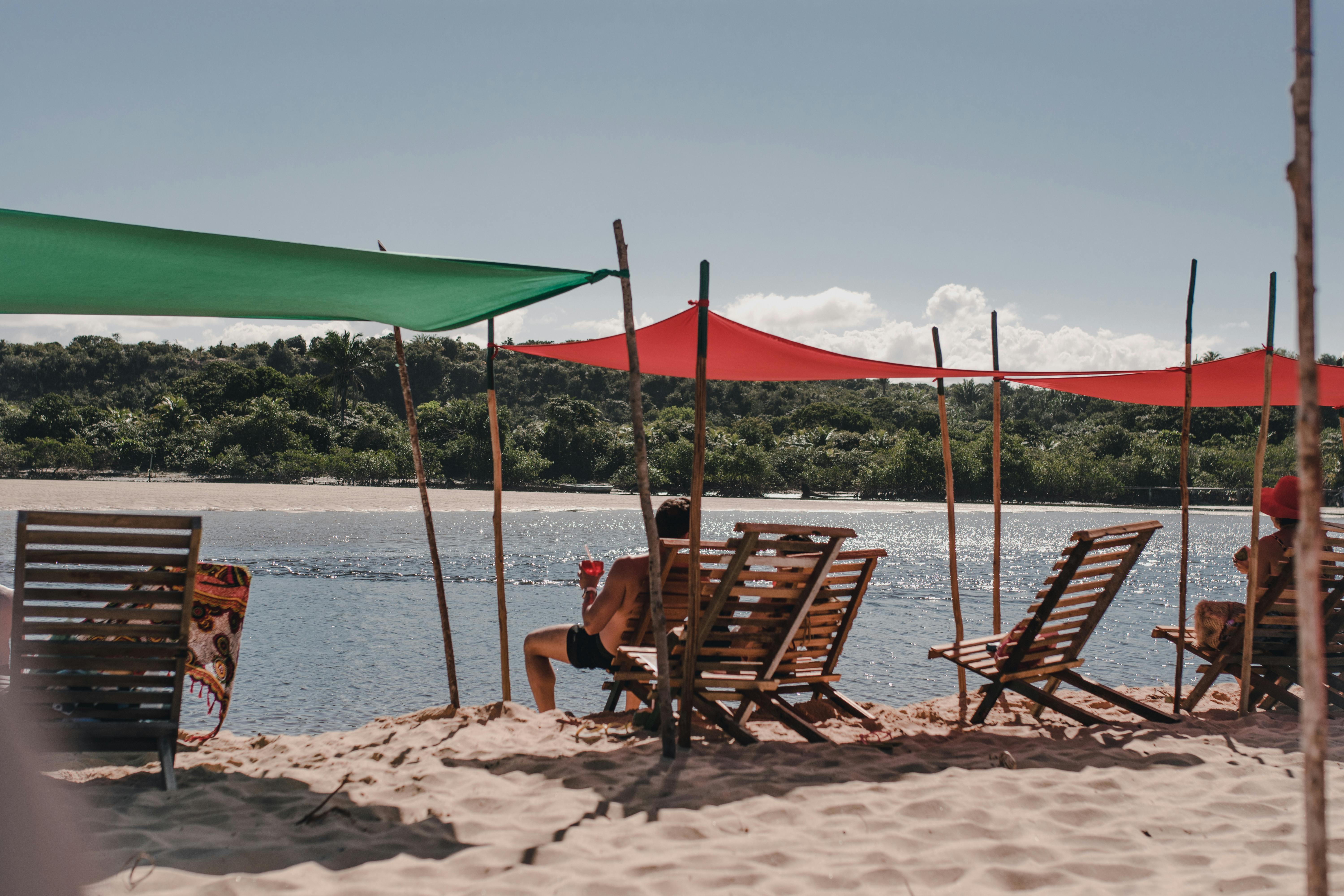 A tranquil scene of people relaxing under colorful sunshades on a sandy beach by the water.