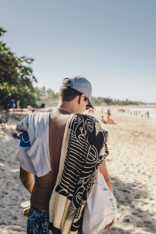 Free Back view of a man on a sandy beach in summer, carrying towels under a clear blue sky. Stock Photo