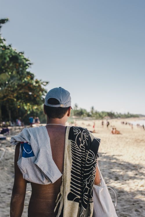 Free A man with towels over his shoulder walking towards the ocean on a sunny beach day. Stock Photo