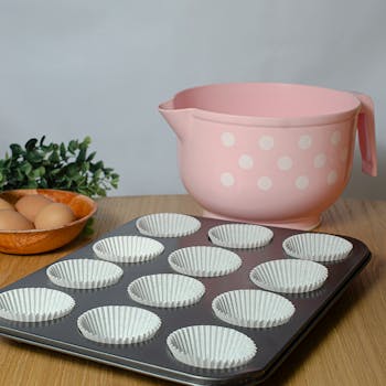 Pink bowl and cupcake tray on wooden surface, perfect for baking themes.
