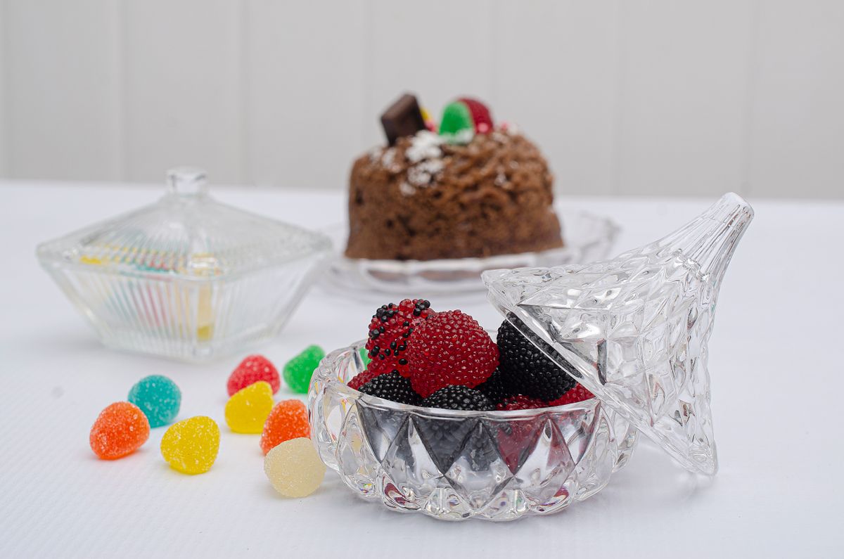 Assorted gummy candies in a glass bowl with a chocolate cake in the background.