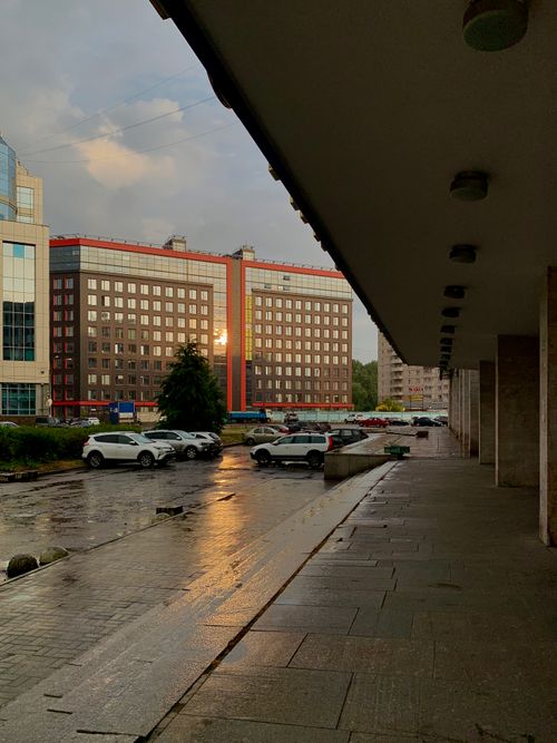 Free Rain-soaked pavement with reflections, cars, and urban buildings in Sankt-Peterburg during sunset. Stock Photo