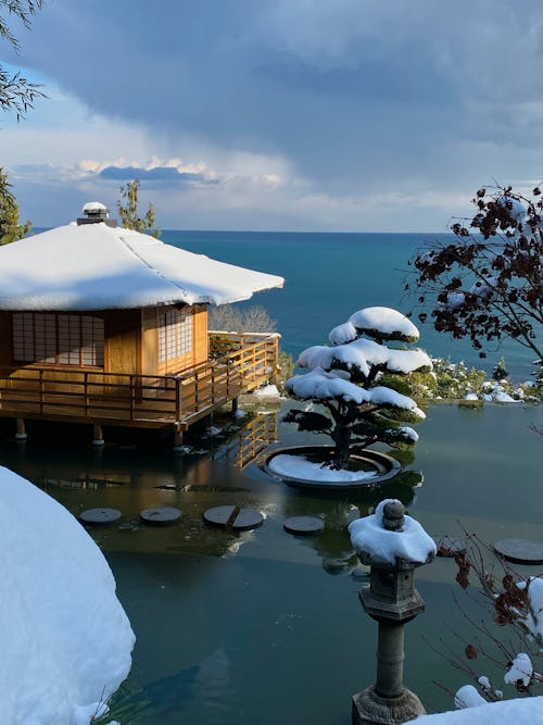 Free Brown Wooden House on Snow Covered Ground Beside Body of Water Stock Photo