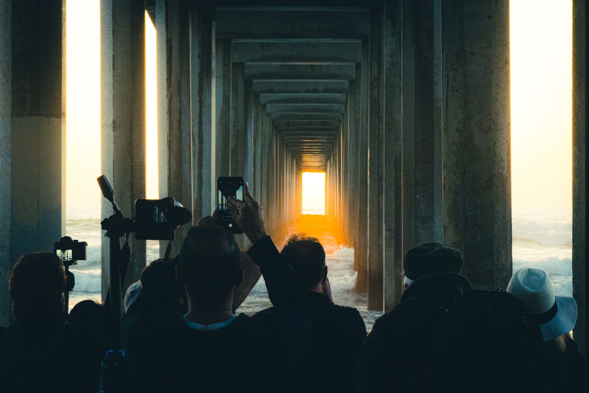 Photographers gather at Scripps Pier, La Jolla, capturing a stunning sunset through the pillars.