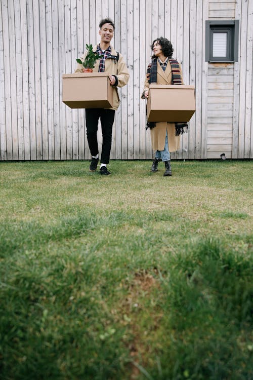 Free A Man and a Woman Carrying Boxes While Walking on the Green Grass Stock Photo