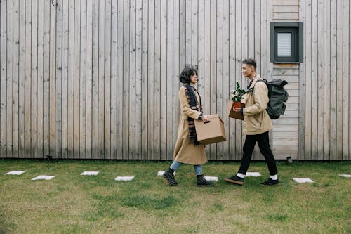 A Couple Walking on the Green Grass While Carrying Boxes