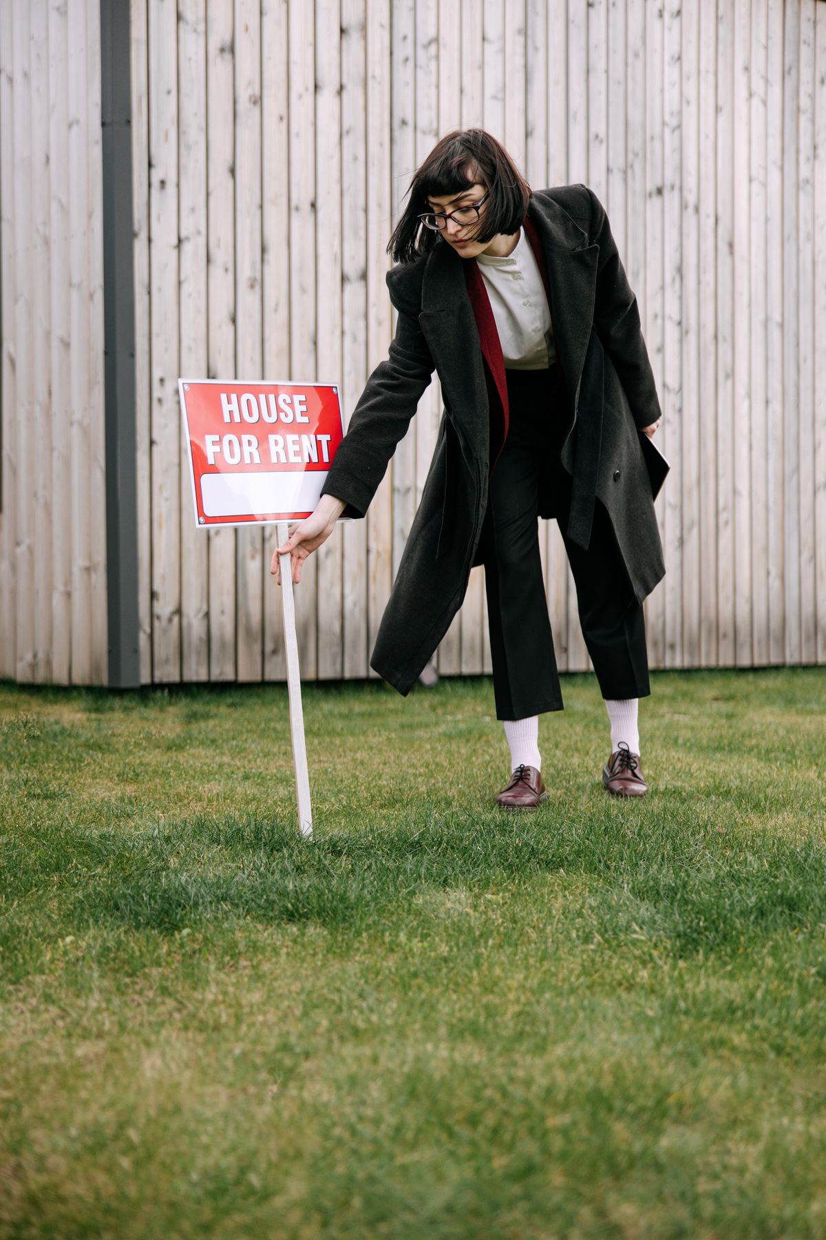 A real estate agent checks a house for rent sign on a lawn near a wooden house.