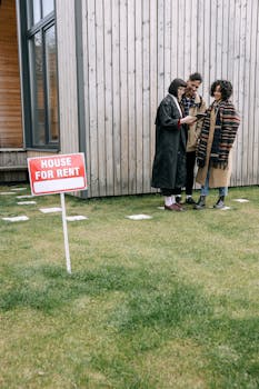 A group of three people reviewing a tablet near a 'House for Rent' sign outside.