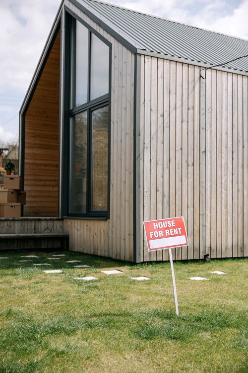 Free A contemporary wooden house with a prominent 'House for Rent' sign on the lawn. Stock Photo