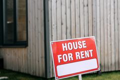 Red 'House for Rent' sign in front of a modern wooden house exterior.