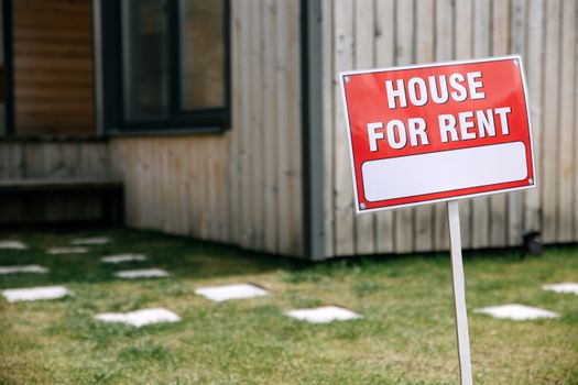 Photo by Ivan S A modern wooden house with a prominent 'House for Rent' sign in the green yard.