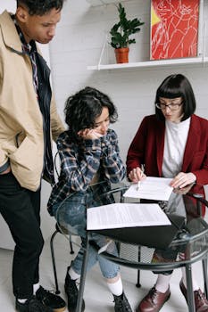 Three individuals reviewing paperwork at a round table indoors.