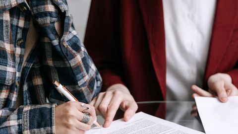Two women reviewing and signing documents together at a glass table indoors.