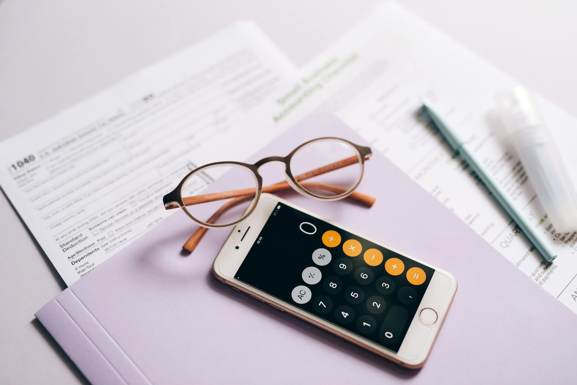 A smartphone calculator and glasses on tax documents, representing modern tax preparation.