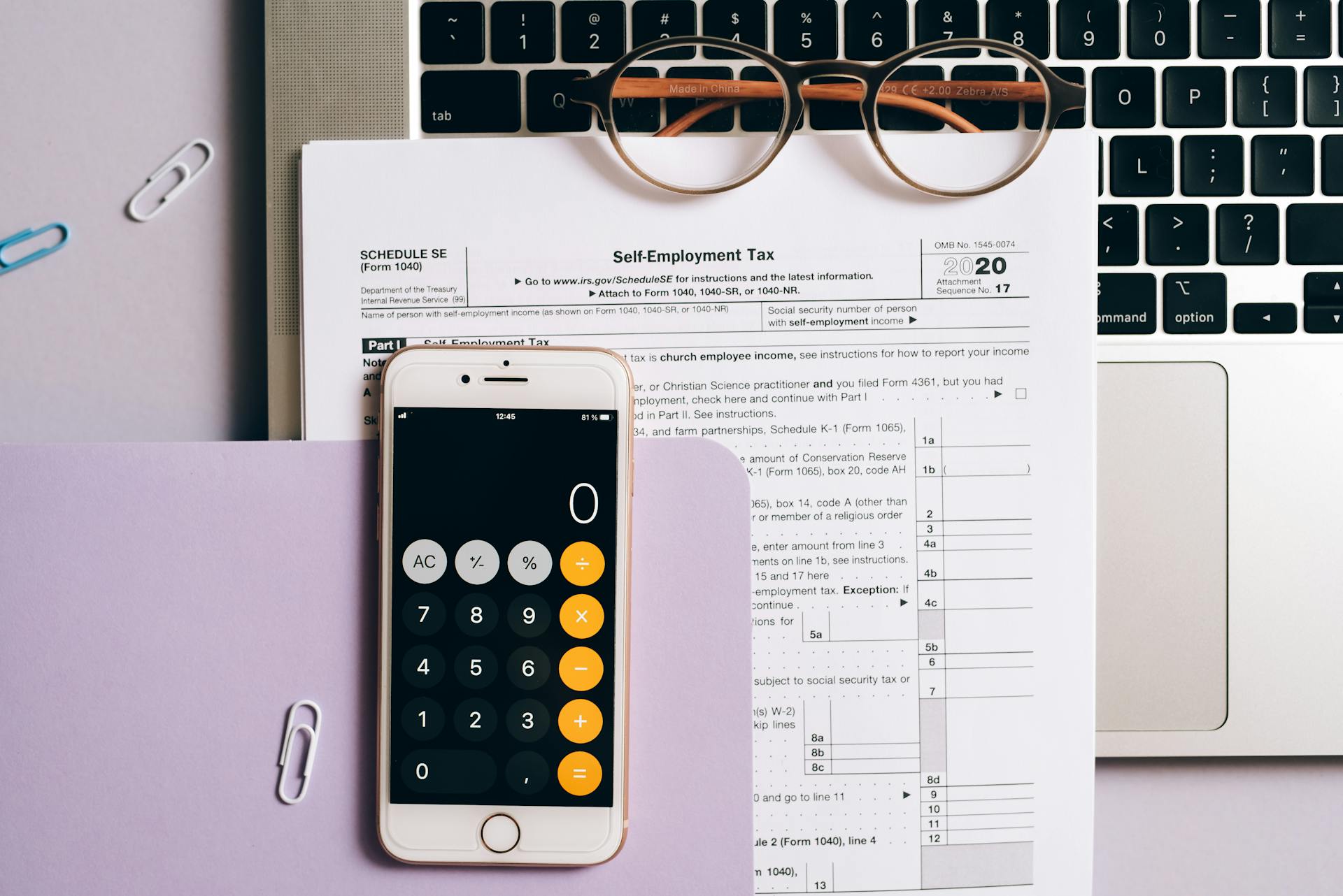 Flat lay of tax documents, smartphone calculator, and laptop for self-employment accounting.