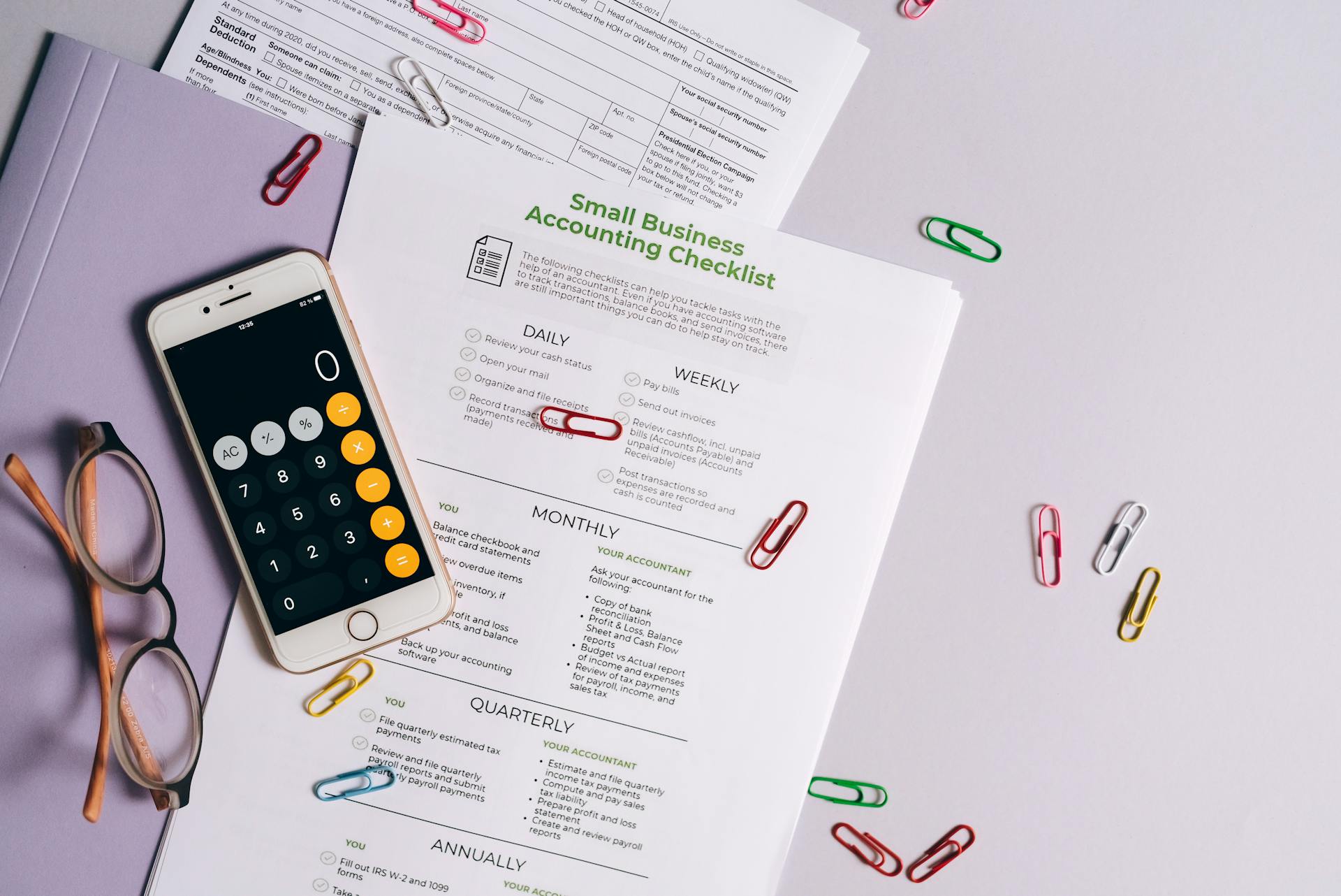 Top view of accounting essentials including smartphone, eyeglasses, and paperwork.