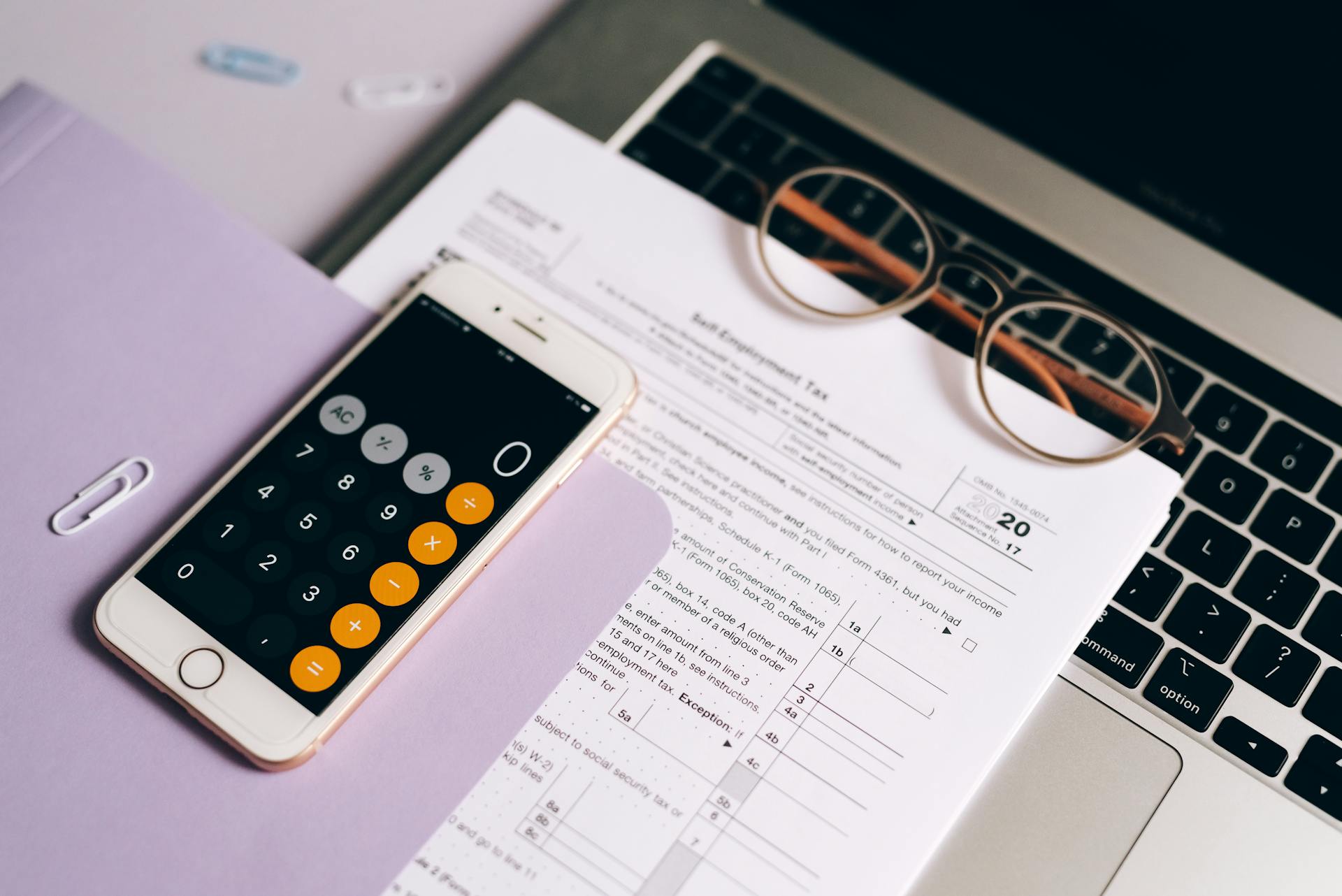 A smartphone with a calculator app on tax documents next to a laptop, emphasizing modern accounting.