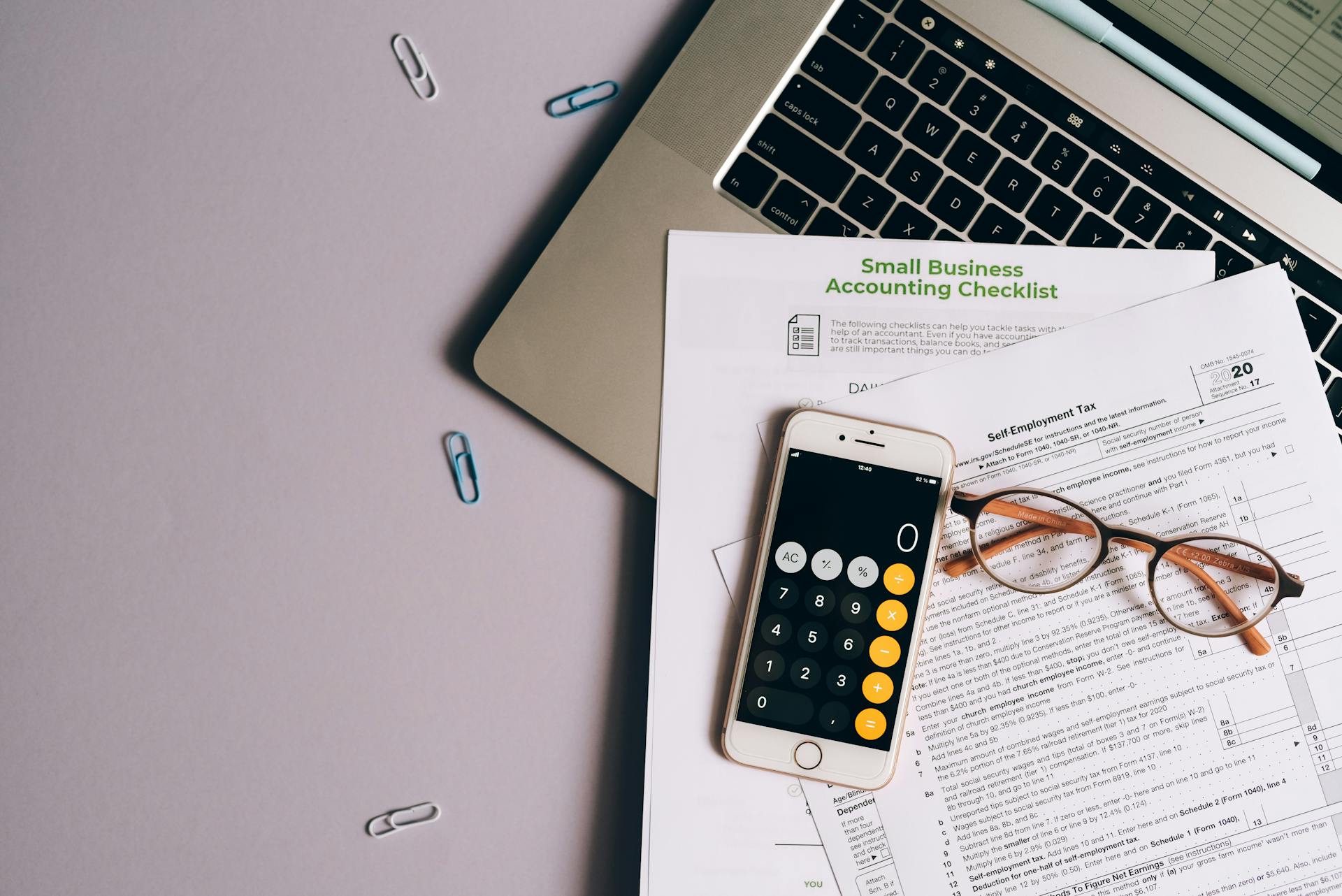 Flat lay of small business accounting tools including tax form, phone, and glasses on a desk.