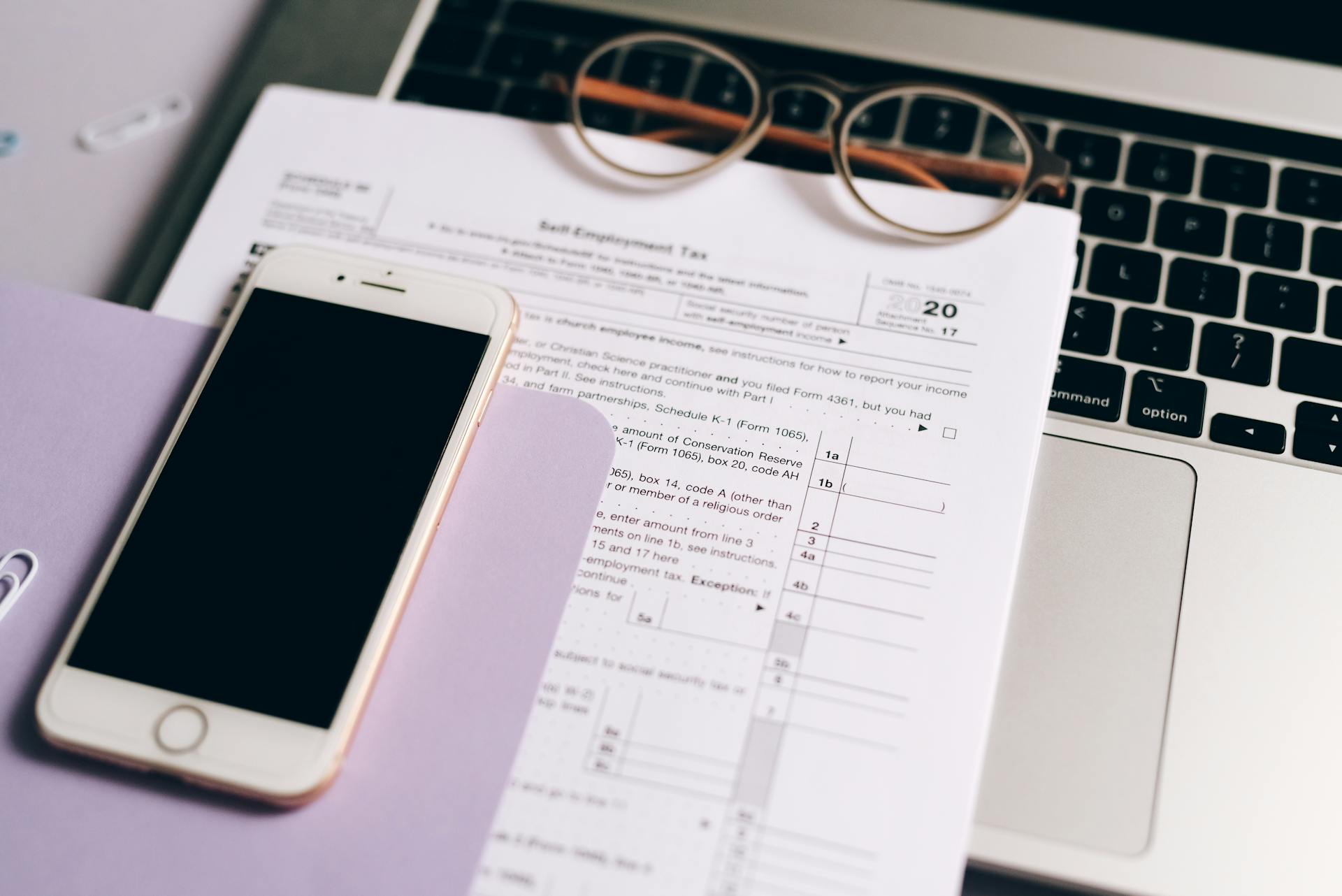 Close-up of tax documents with laptop and smartphone on a desk.