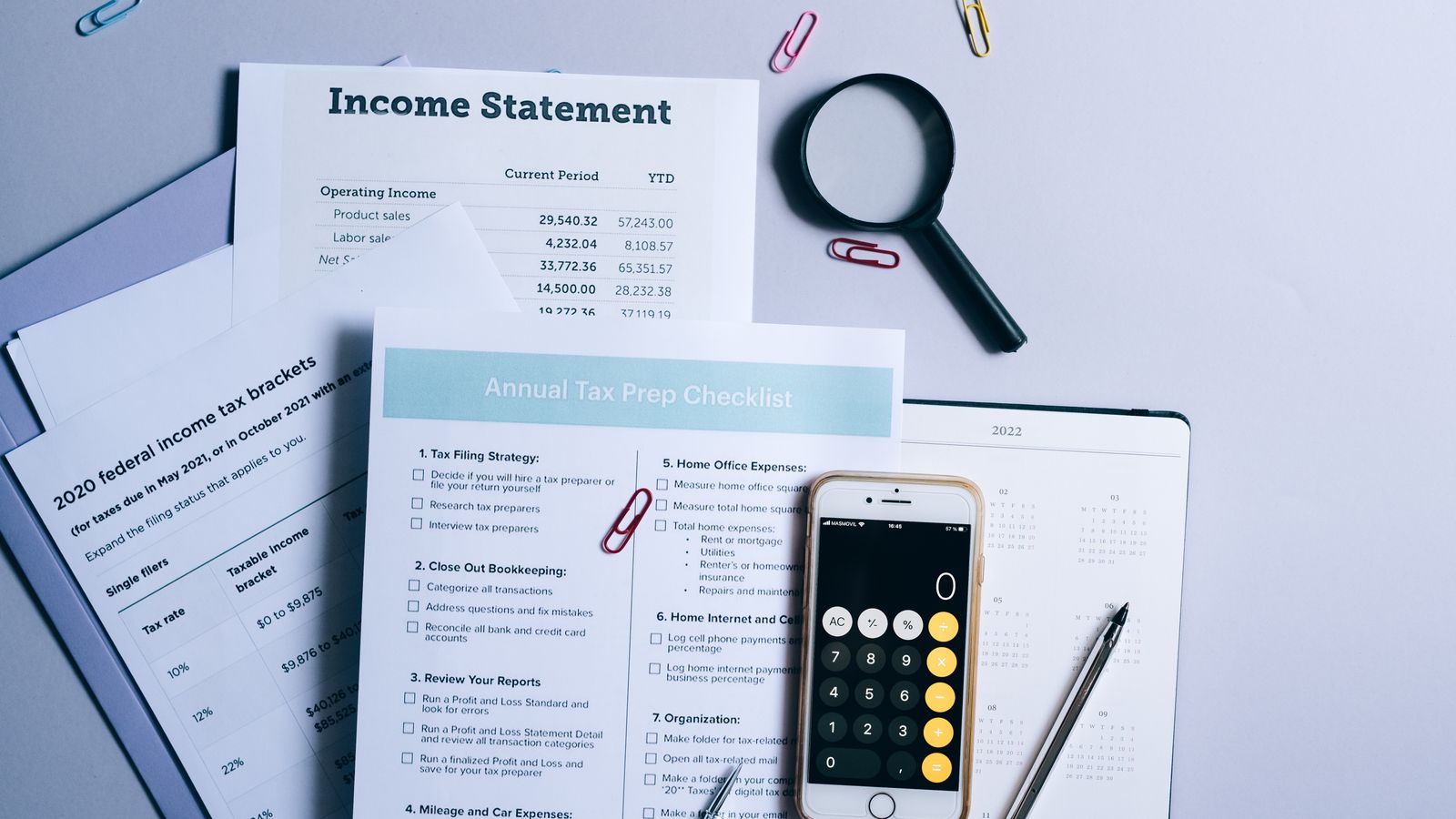 An organized desk with tax documents, checklist, and gadgets for tax preparation.