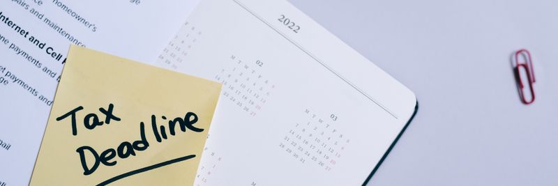A sticky note highlights tax deadline on a calendar alongside documents, emphasizing financial planning.