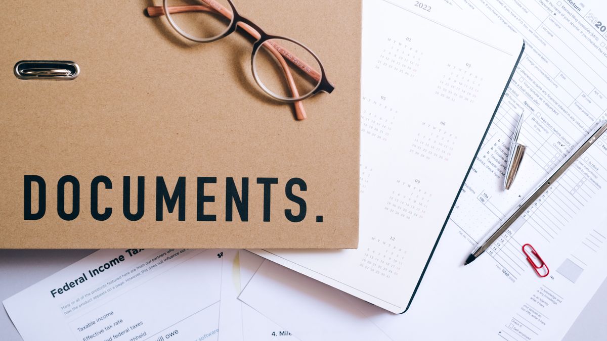 Flat lay of office supplies including documents, calendar, and eyeglasses on a desk.