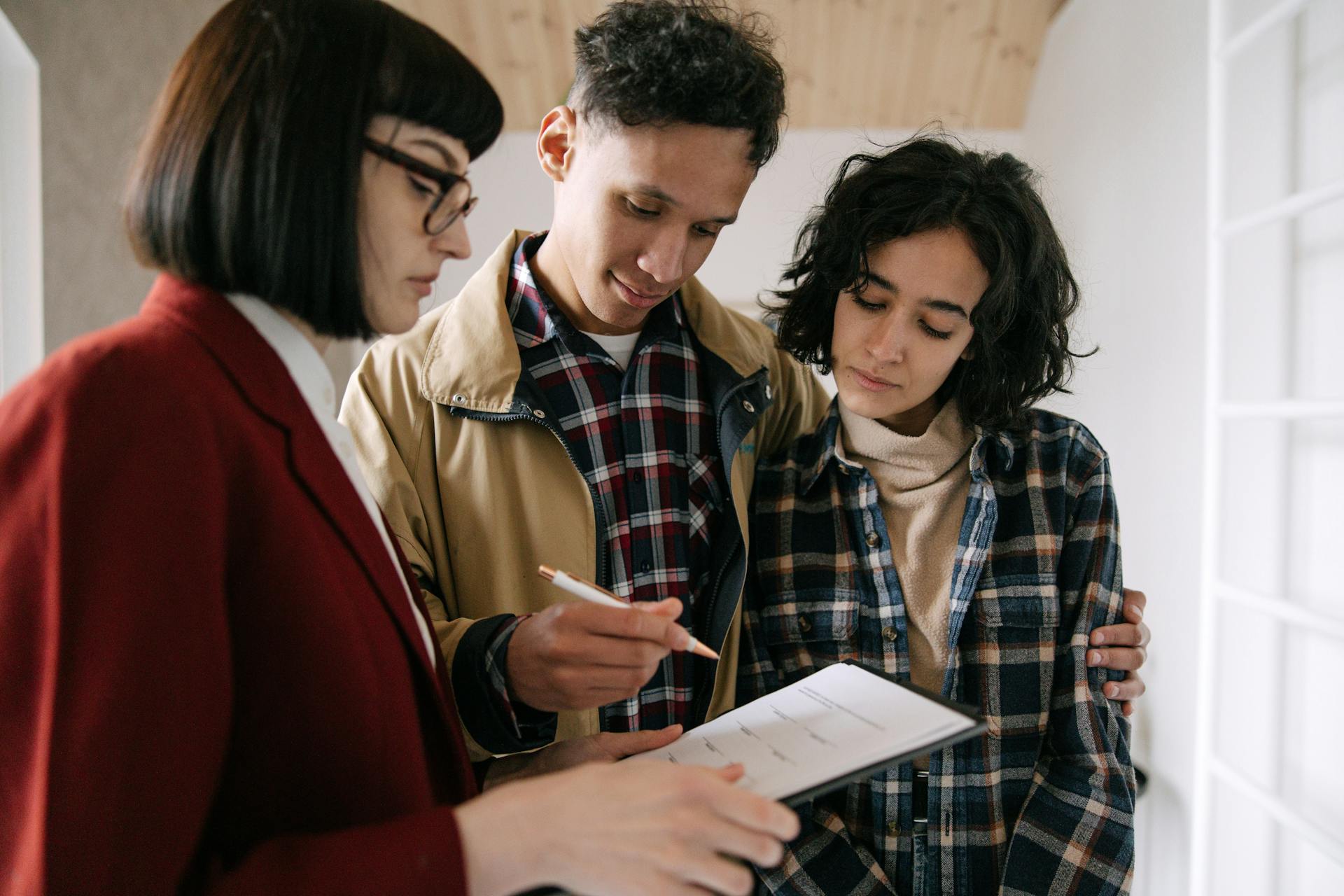 A young couple consults with a real estate agent about documents inside an apartment.