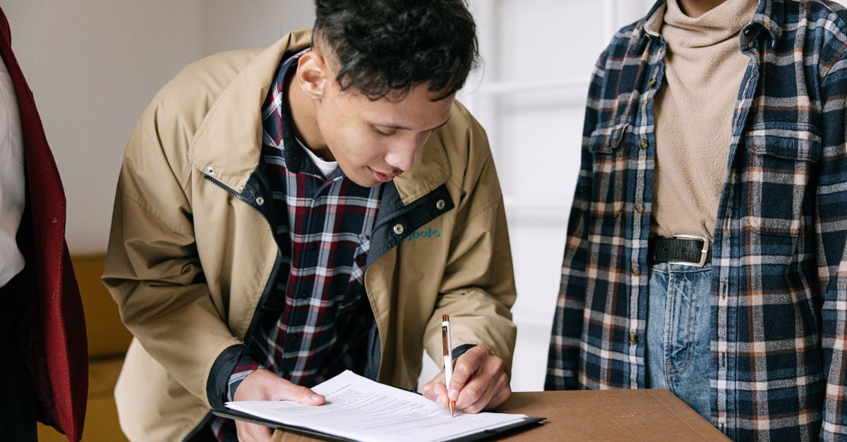 Young adults signing documents on moving day, finalizing new home purchase.