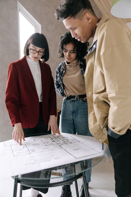 Achieving Soc 2 Compliance For Smb Architecture Firms 2 - Achieving Soc 2,Soc 2 Compliance Guide For Small Architecture Firms - - Bonelli Systems A Real Estate Agent Discussing Blueprints With A Young Couple At A Glass Table Indoors.