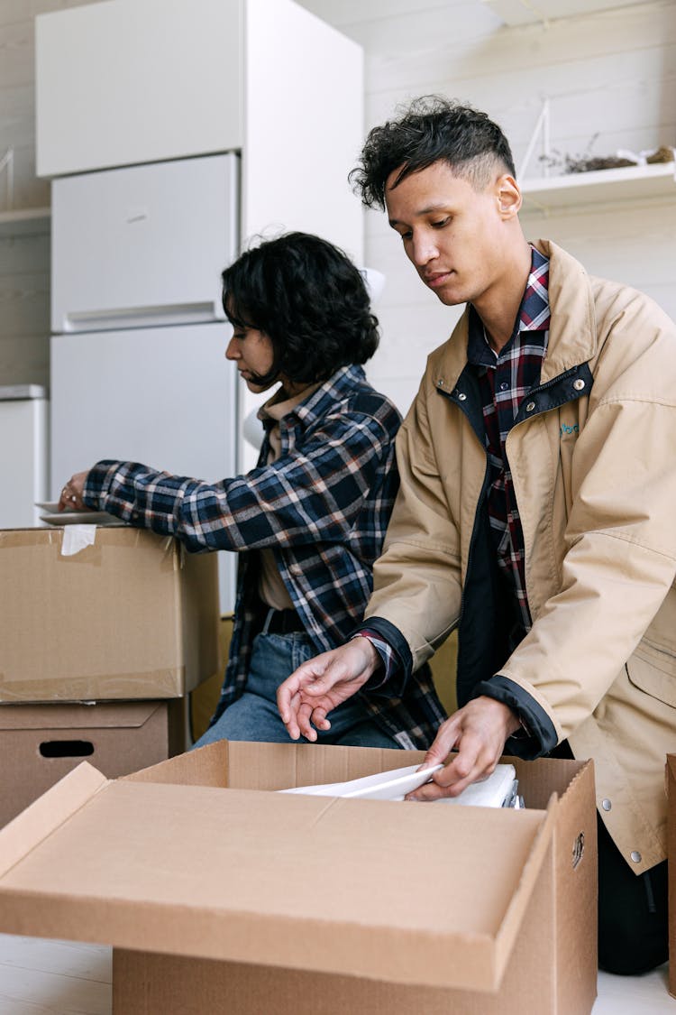 Couple Packing Their Belongings On A Carton Box 