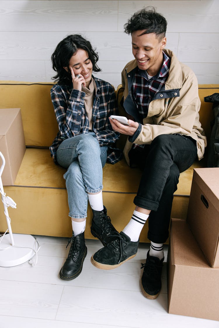 A Couple Sitting On The Couch While Looking At The Phone With Their Legs Crossed