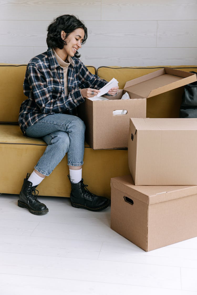 Woman Sitting On A Sofa And Unpacking Boxes 