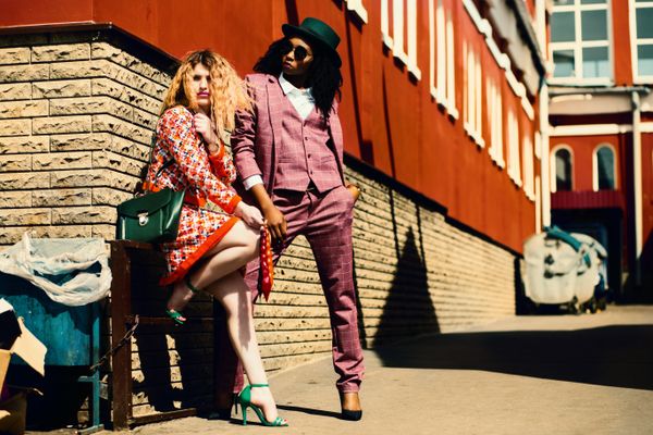 Two people posed against a painted brick wall with bags — photo by Godisable Jacob on Pexels